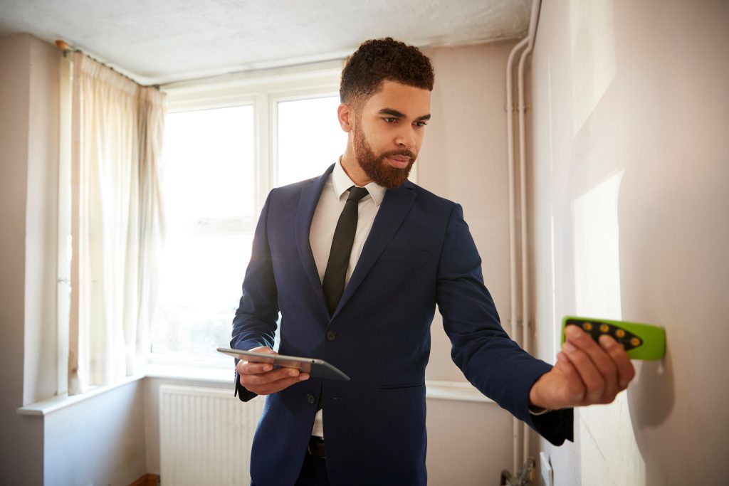 Male Realtor With Digital Tablet Measuring Room With Laser Measure