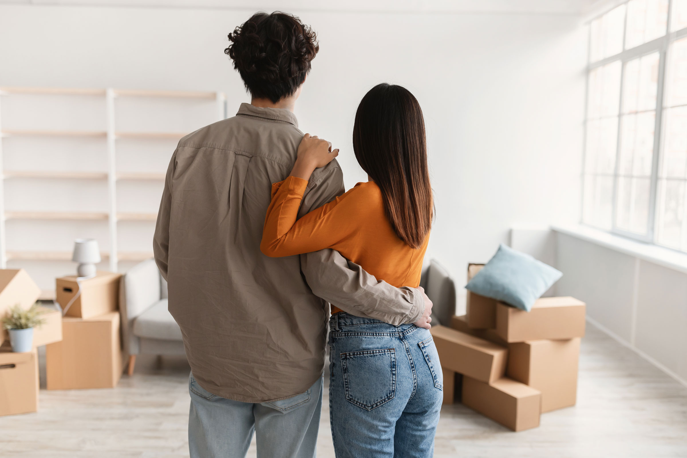 Couple standing in a mostly empty white living room, facing away from the camera.
